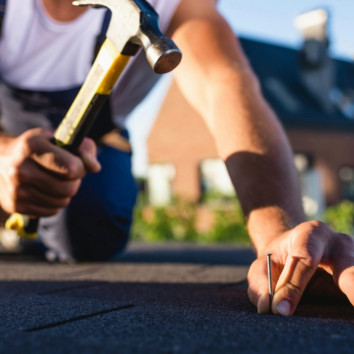 Cropped view of builder holding hummer and nail while repairing roof of building